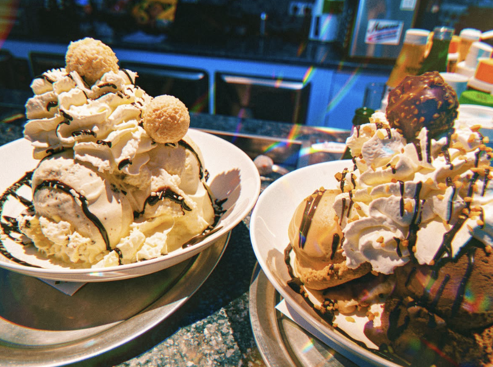 Zwei opulente Eisbecher mit Sahne, Schokosoße und Raffaello- bzw. Ferrero-Rocher-Topping